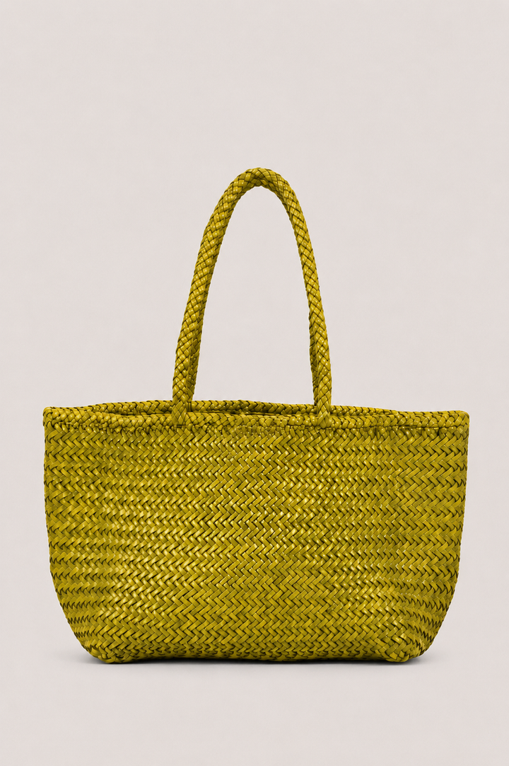 A woven straw tote bag in a vibrant olive yellow-green color, featuring two thick braided shoulder straps, set against a solid light gray background.